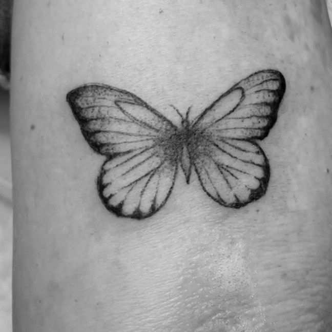 Fein schattierter, symmetrischer Schmetterling als Tattoo auf einem Arm.